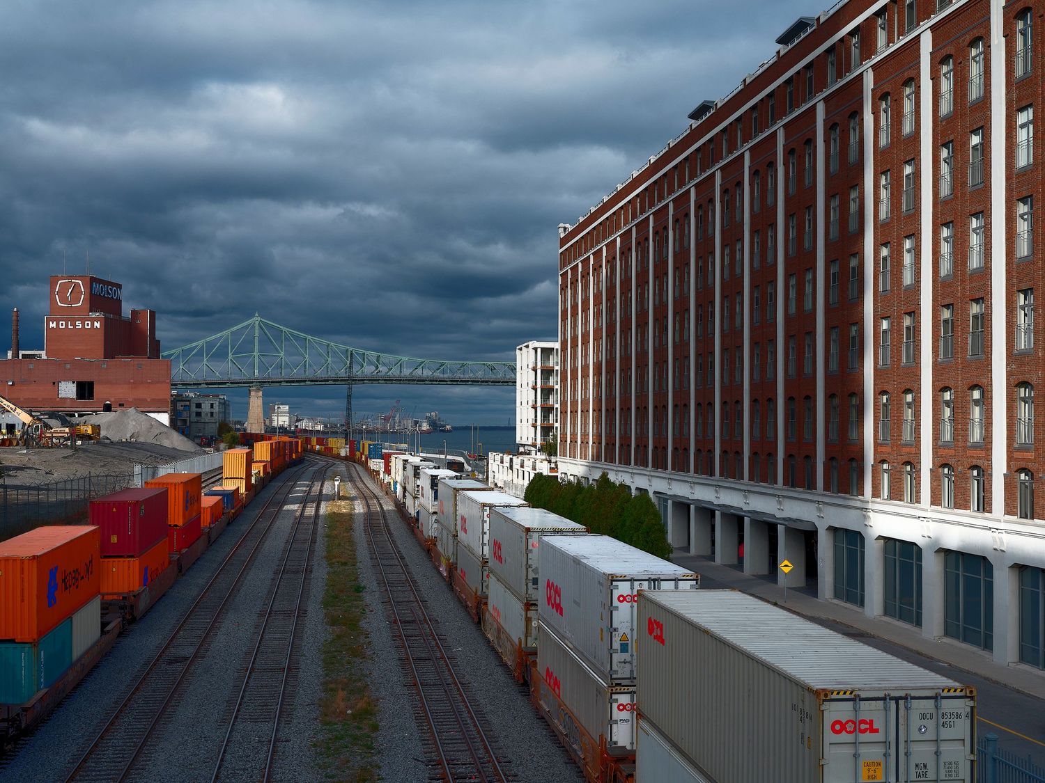 Industrial waterfront buildings and warehouses line a harbor with dramatic cloudy skies overhead.