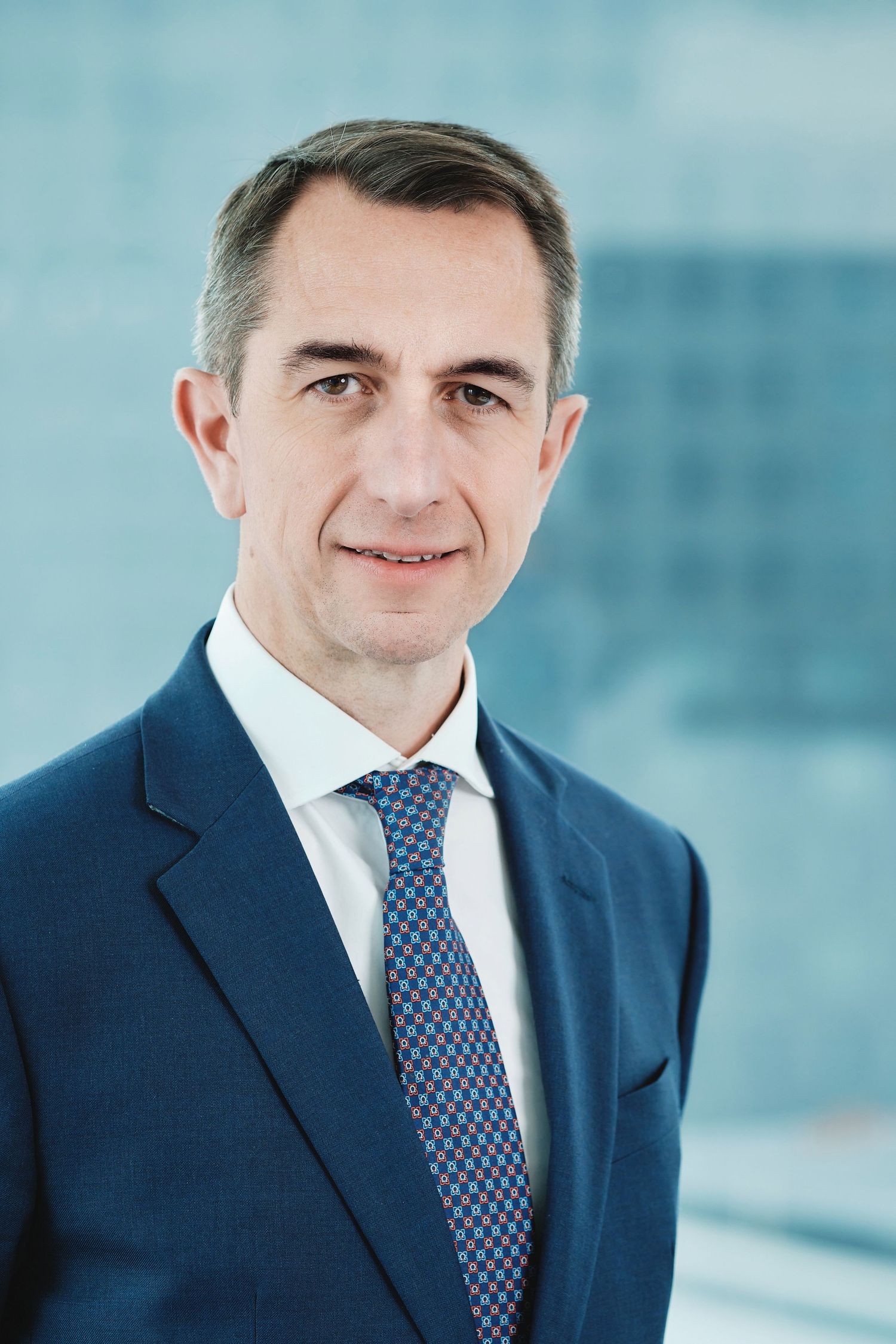 Professional business portrait showing executive in navy suit and patterned tie.