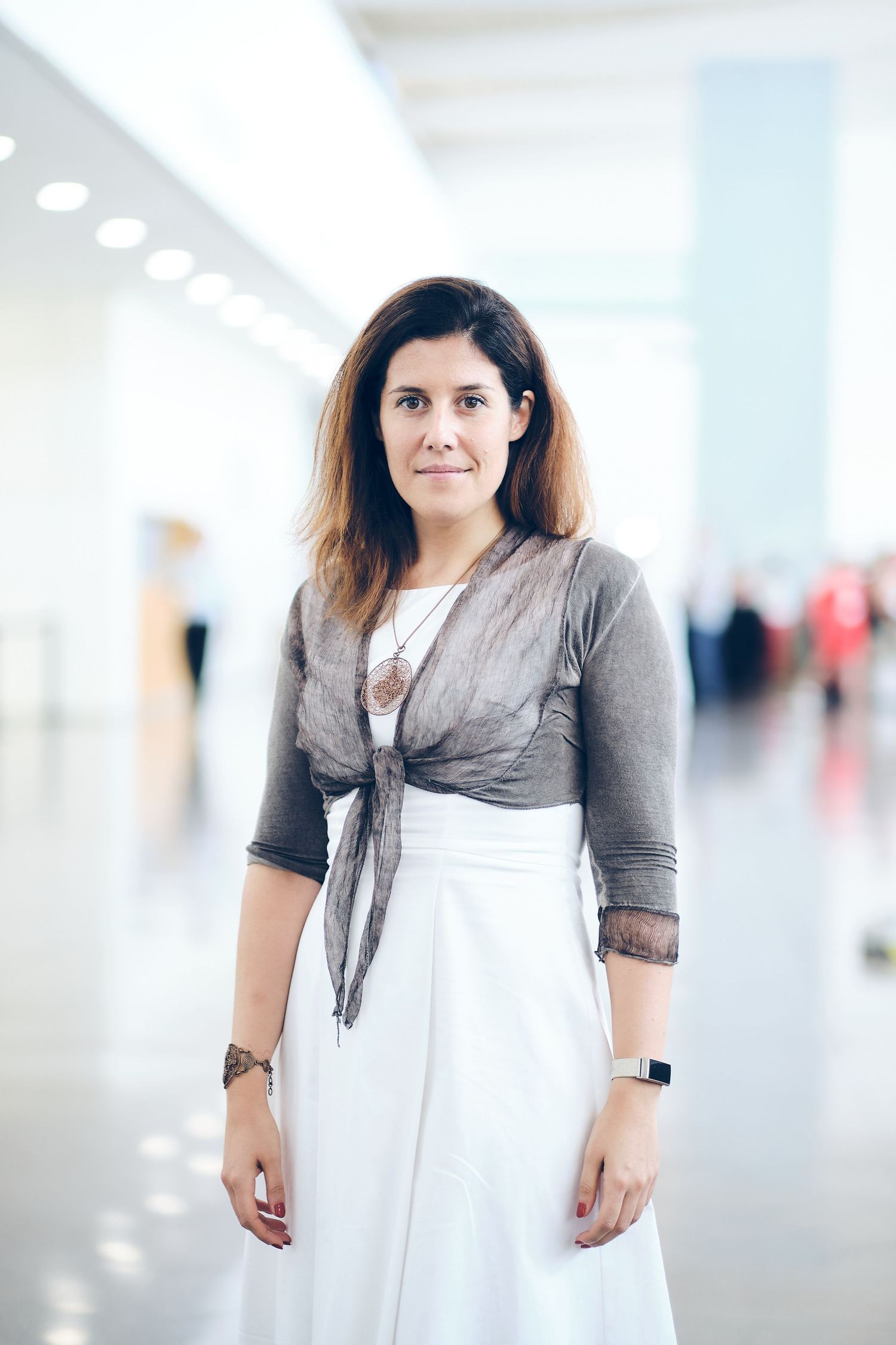 Professional portraits of person wearing white dress and gray wrap in bright hallway.