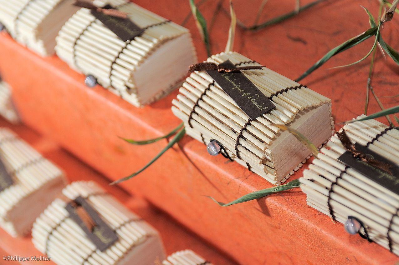 Handmade bamboo wrapped favor boxes tied with ribbon displayed on an orange surface for a rustic wedding celebration.