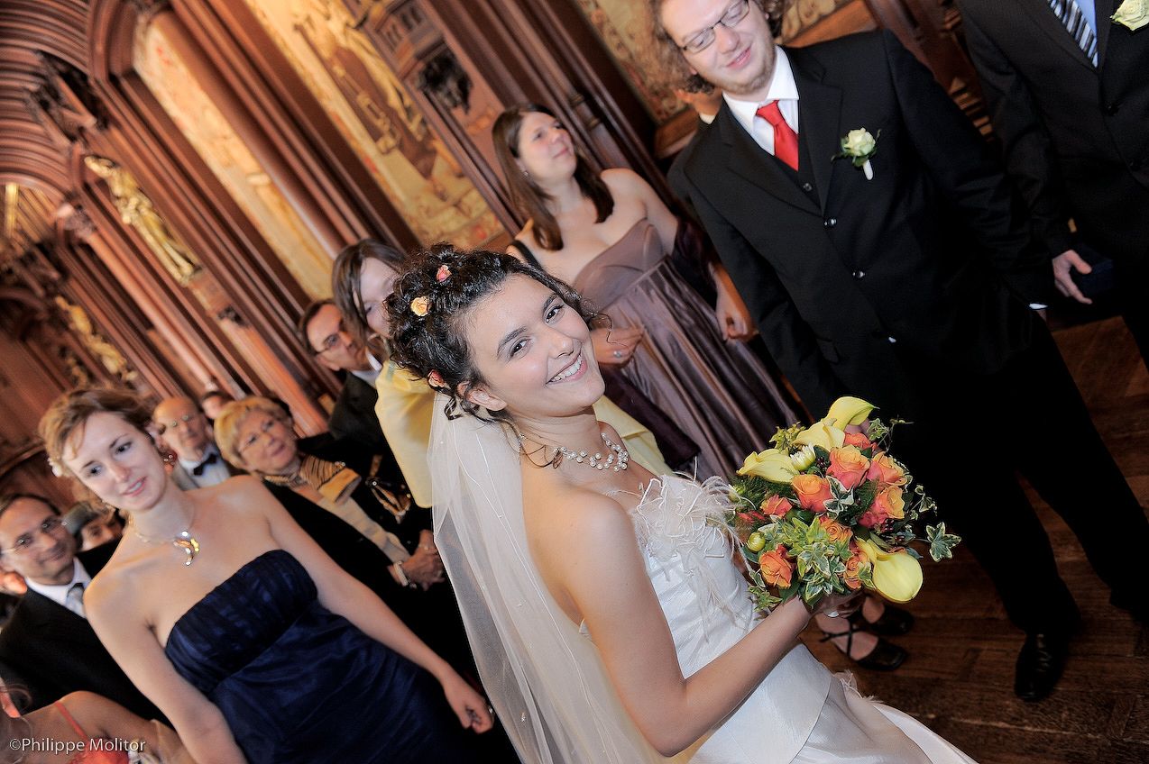 Smiling bride holding colorful bouquet walks down aisle at elegant wedding ceremony with guests in background.