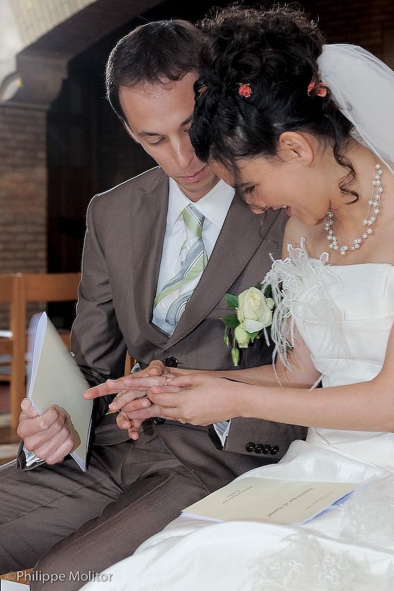 Bride and groom examining wedding rings during ceremony, wearing formal attire in a church setting.