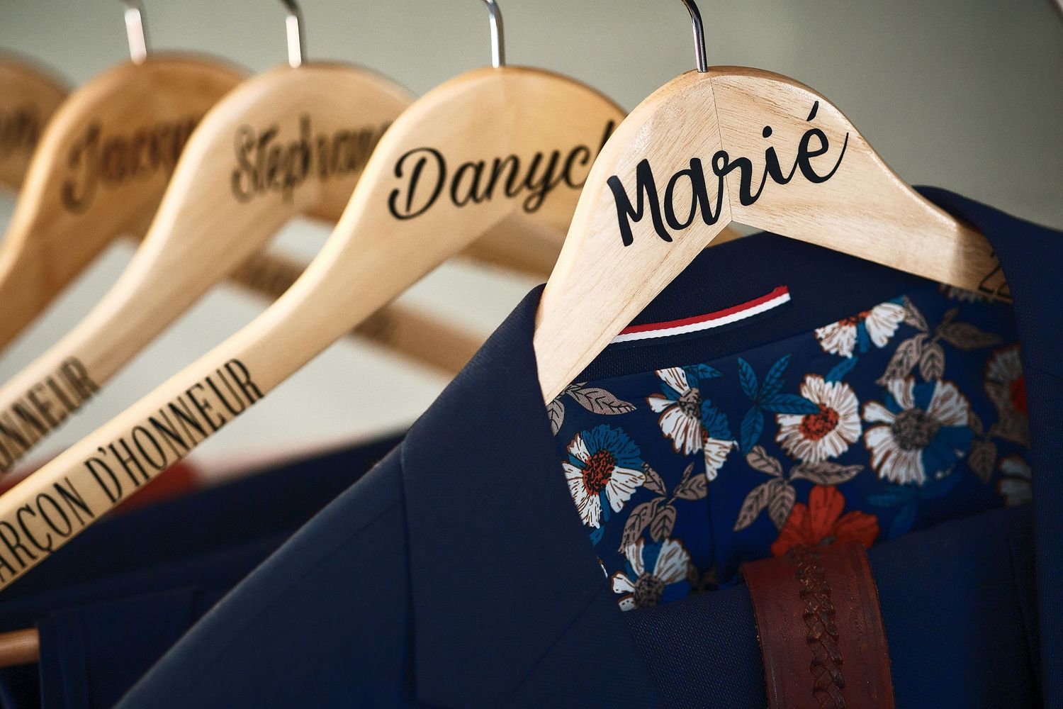 Personalized wooden wedding hangers labeled Marié and groomsmen roles, holding navy suits with floral ties.