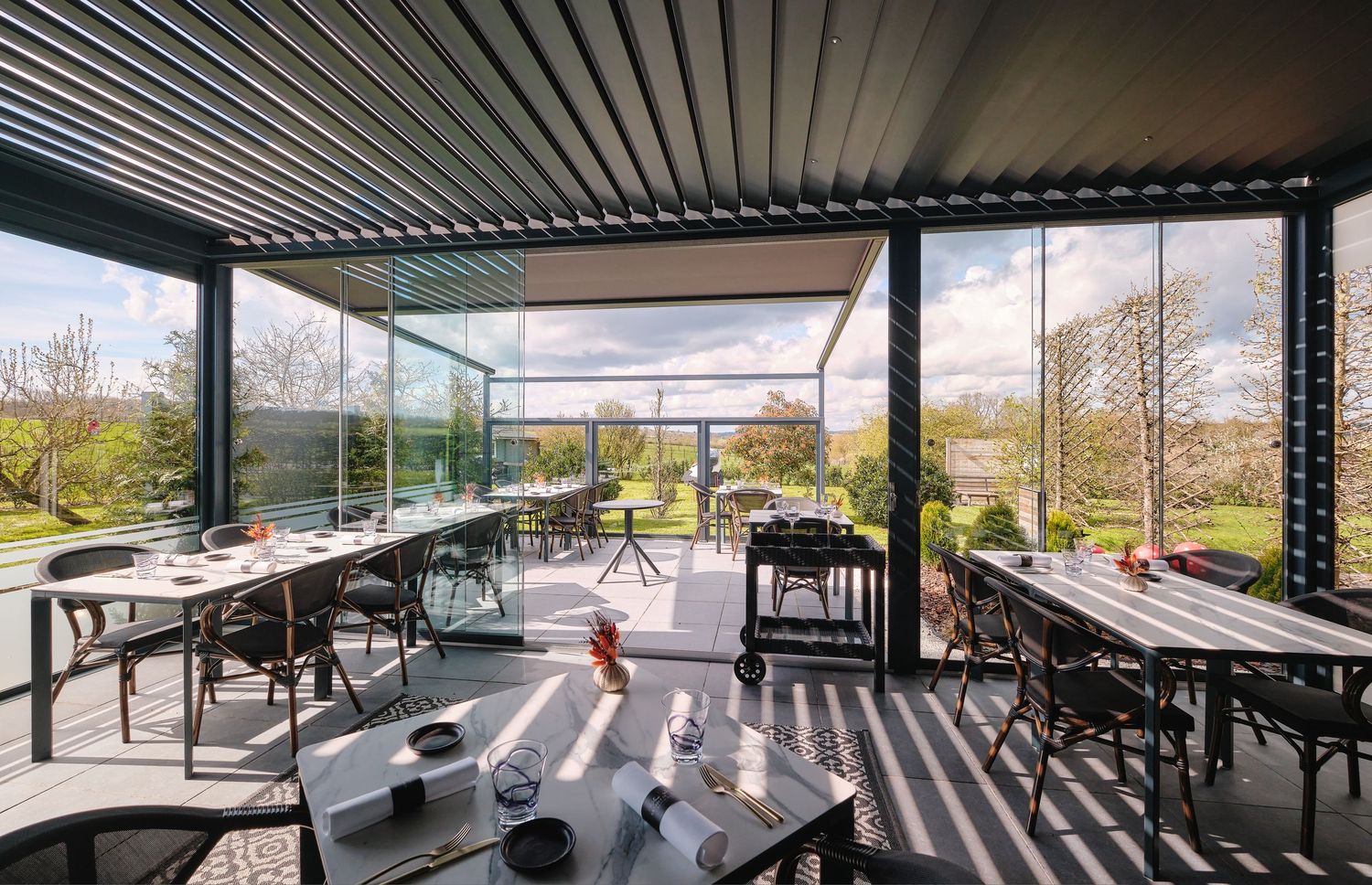 Covered outdoor dining terrace with slatted roof and panoramic views of surrounding landscape.