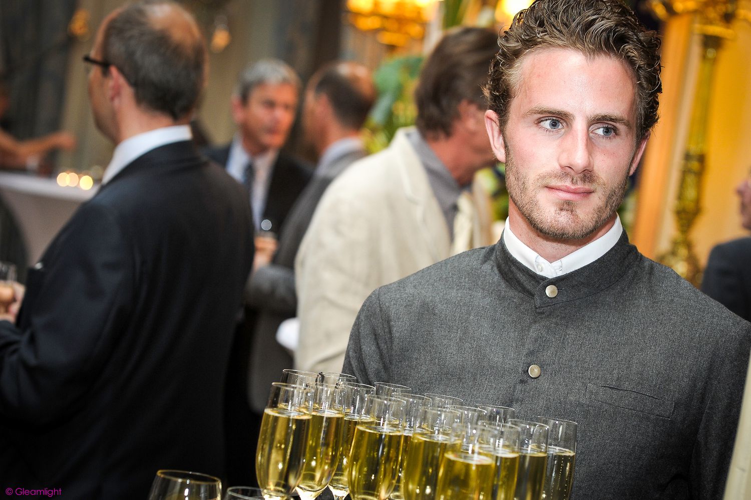 Evening reception with drinks being served on golden-lit trays.