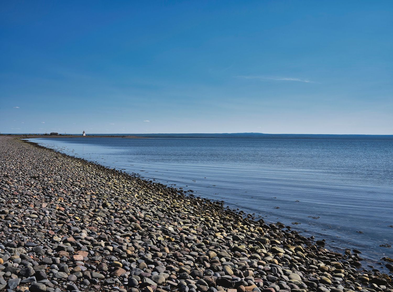 Rocky seawall stretching along calm blue waters under clear sky.