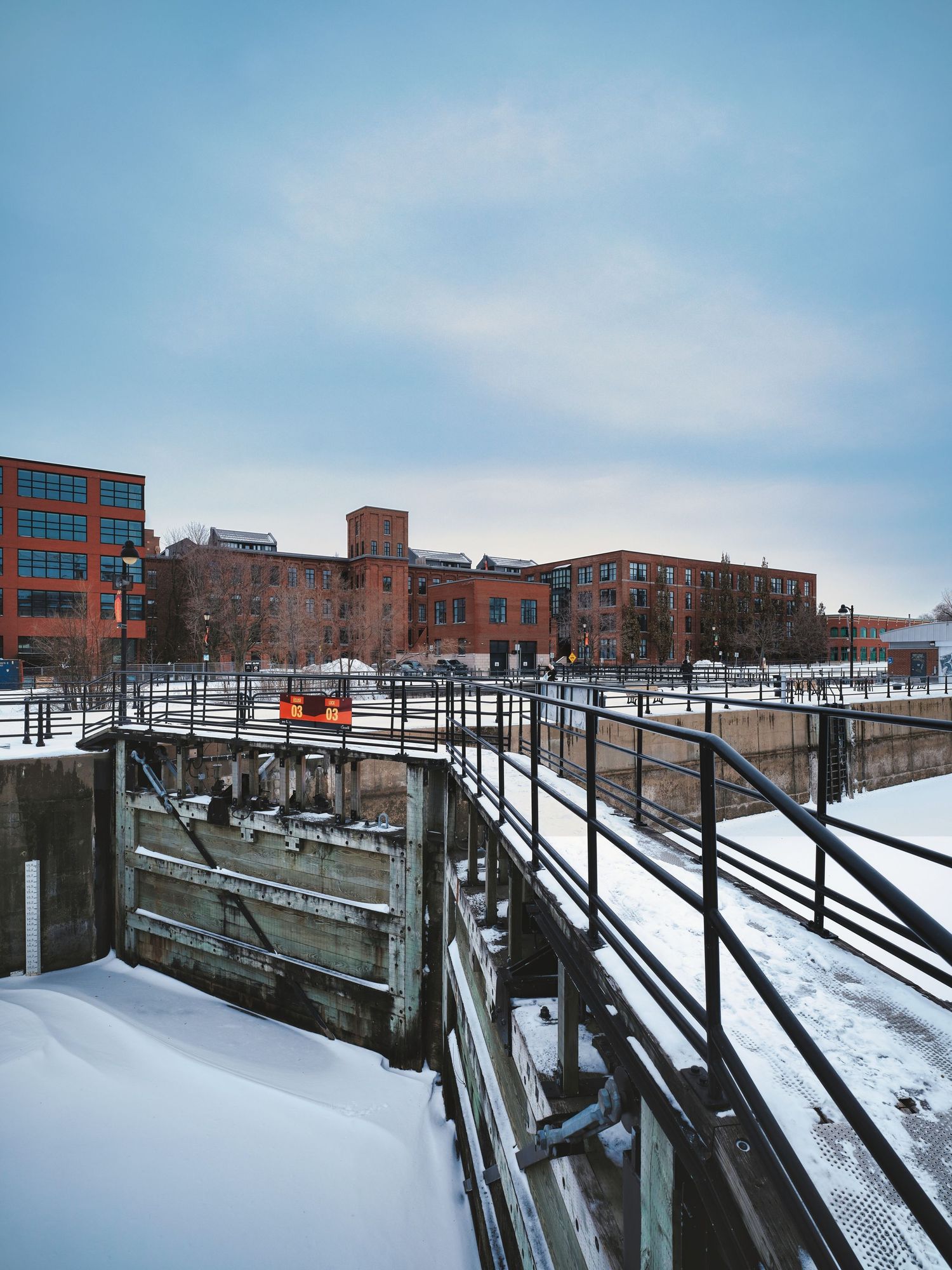 Snow-covered industrial brick buildings and railway tracks in an urban setting under a pale winter sky.