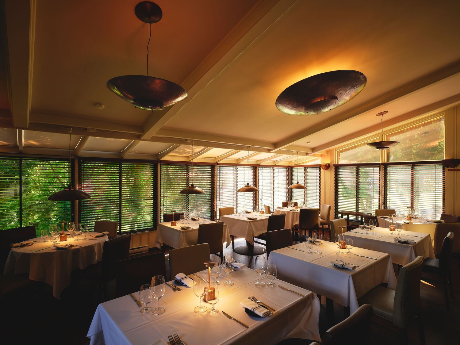 Modern restaurant interior with panoramic windows and elegant dining setup in warm lighting.