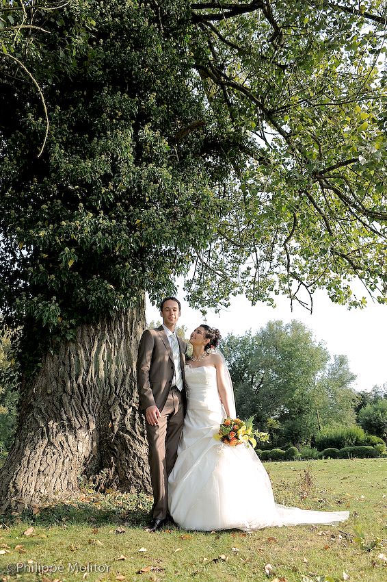 Bride and groom pose together under a large tree in a lush garden on their wedding day.