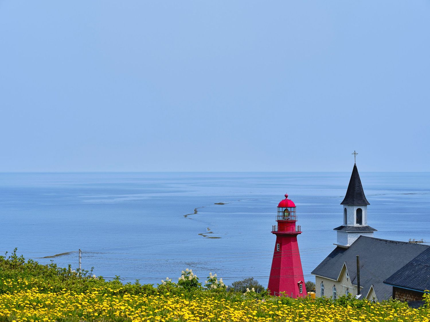 Coastal lighthouse scene with red beacon tower and church building along the ocean shore.
