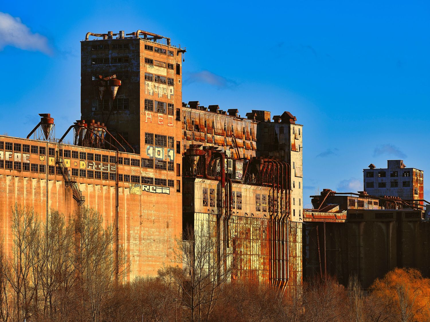 Panoramic view of industrial buildings with rustic brick facades against bright blue sky at sunset.