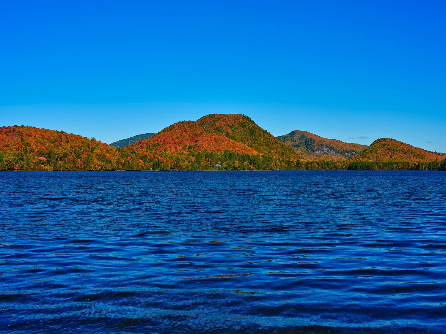 Panoramic view of deep blue lake waters with distant mountains under clear skies.