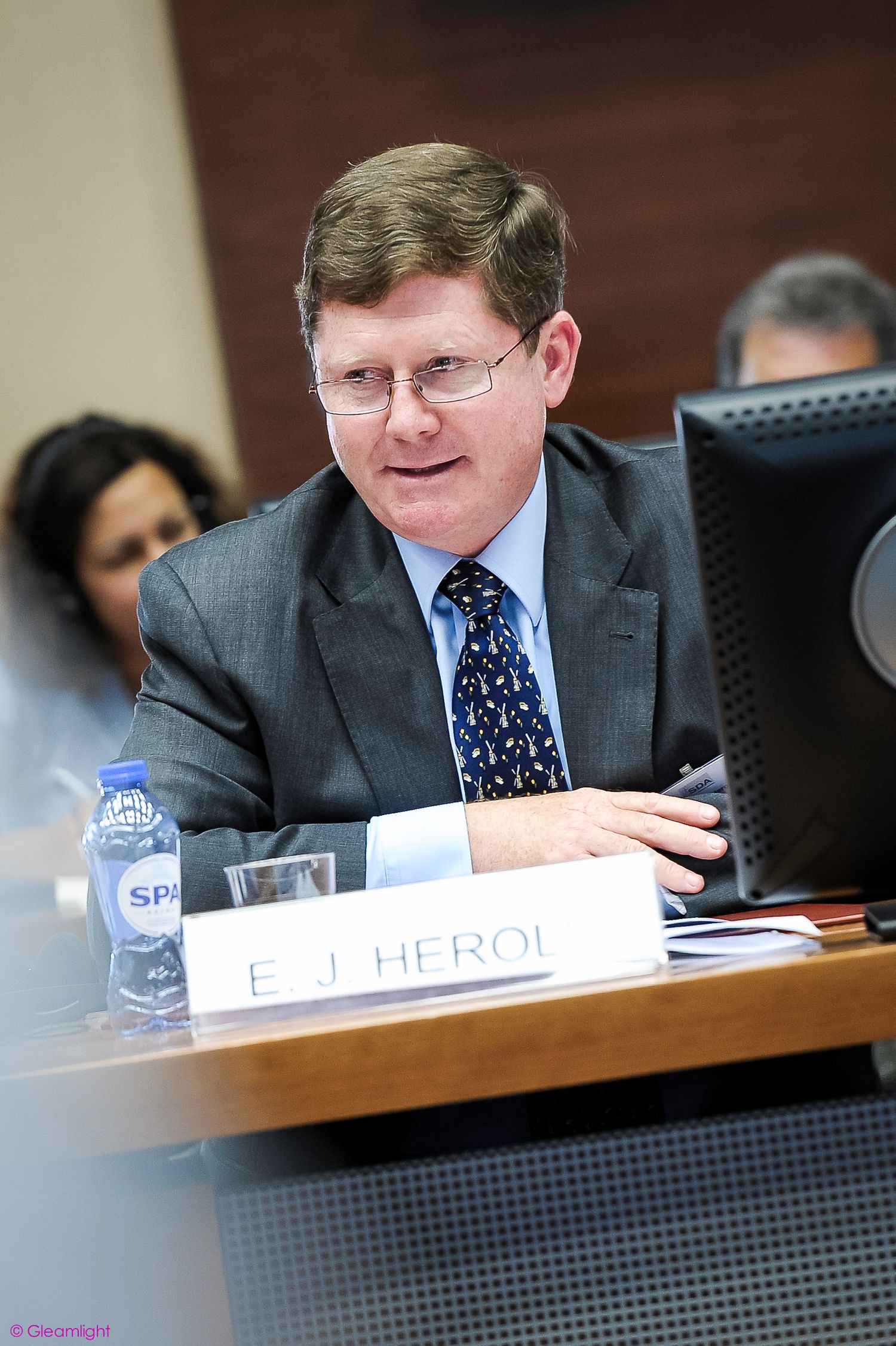 Professional meeting participant in business attire seated at conference table.