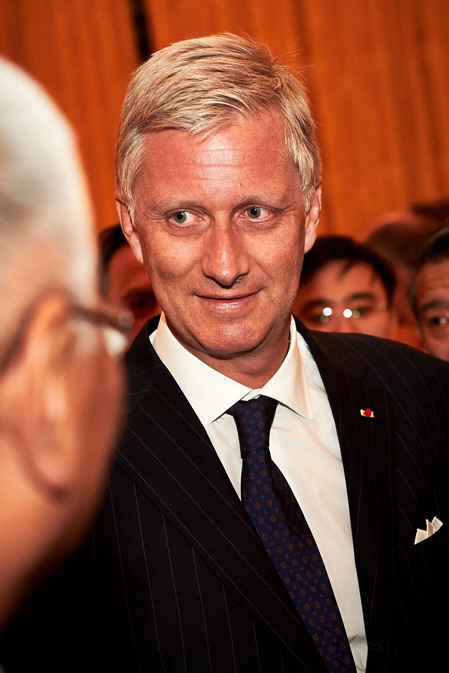 Close-up portrait in formal business attire against orange background.