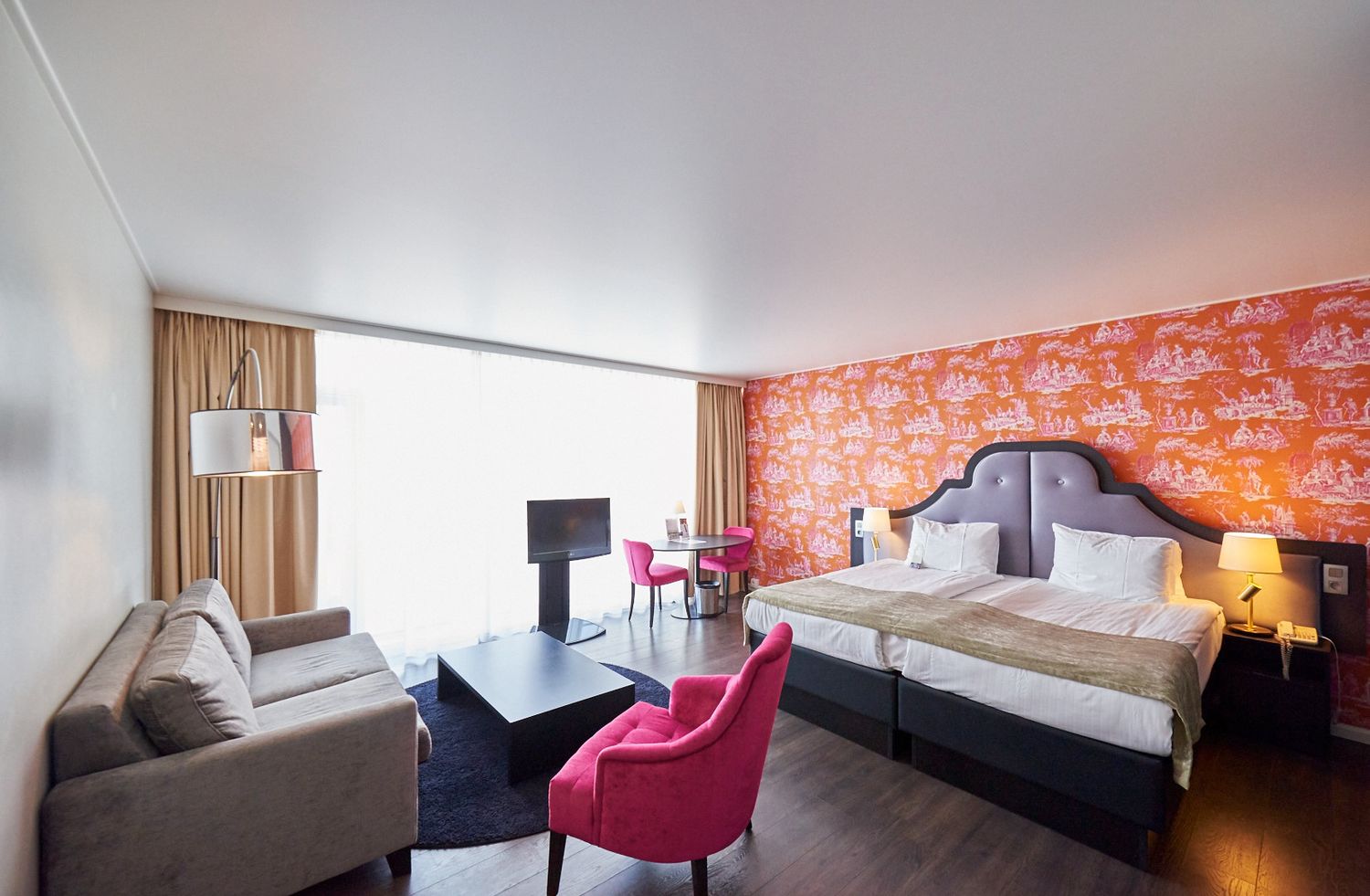 Modern hotel room interior with pink accent wall and contemporary furnishings.