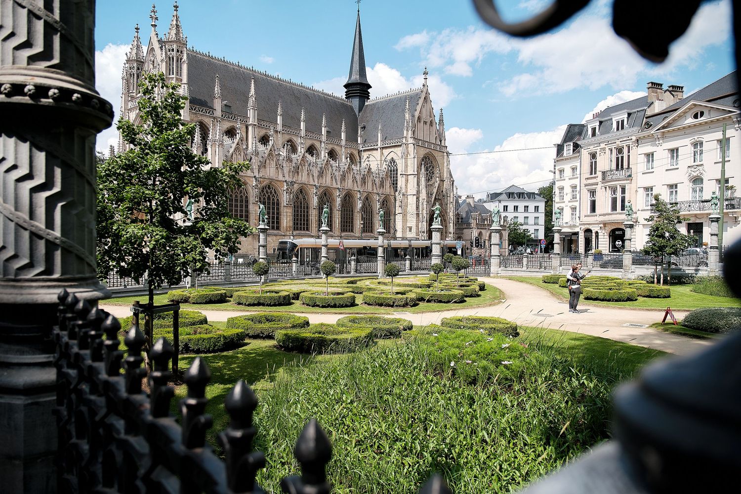 Gothic cathedral overlooks a manicured formal garden with trimmed hedges and tree-lined paths in Brussels, Belgium.