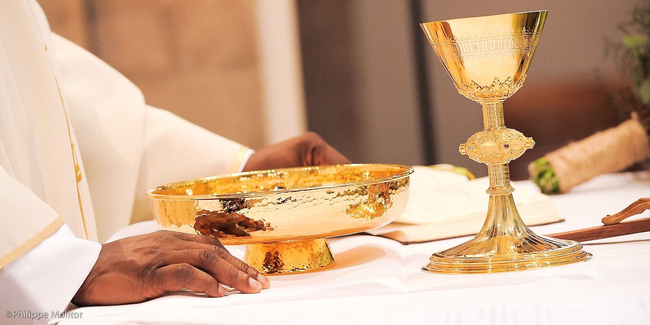 Golden chalice and paten on white altar cloth during Catholic Mass communion ceremony.