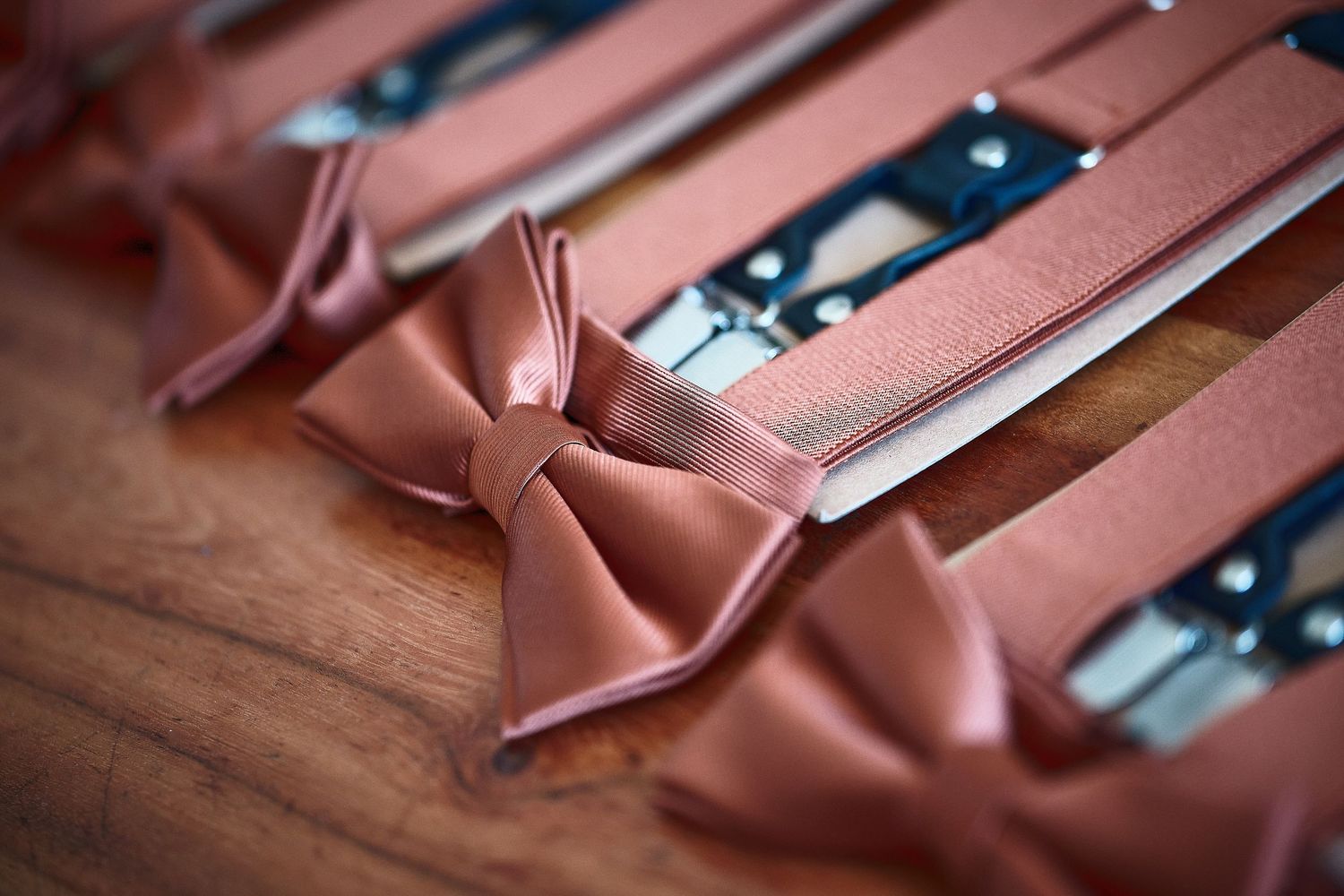 Elegant terracotta bow ties and suspenders arranged on a wooden surface for a wedding party.