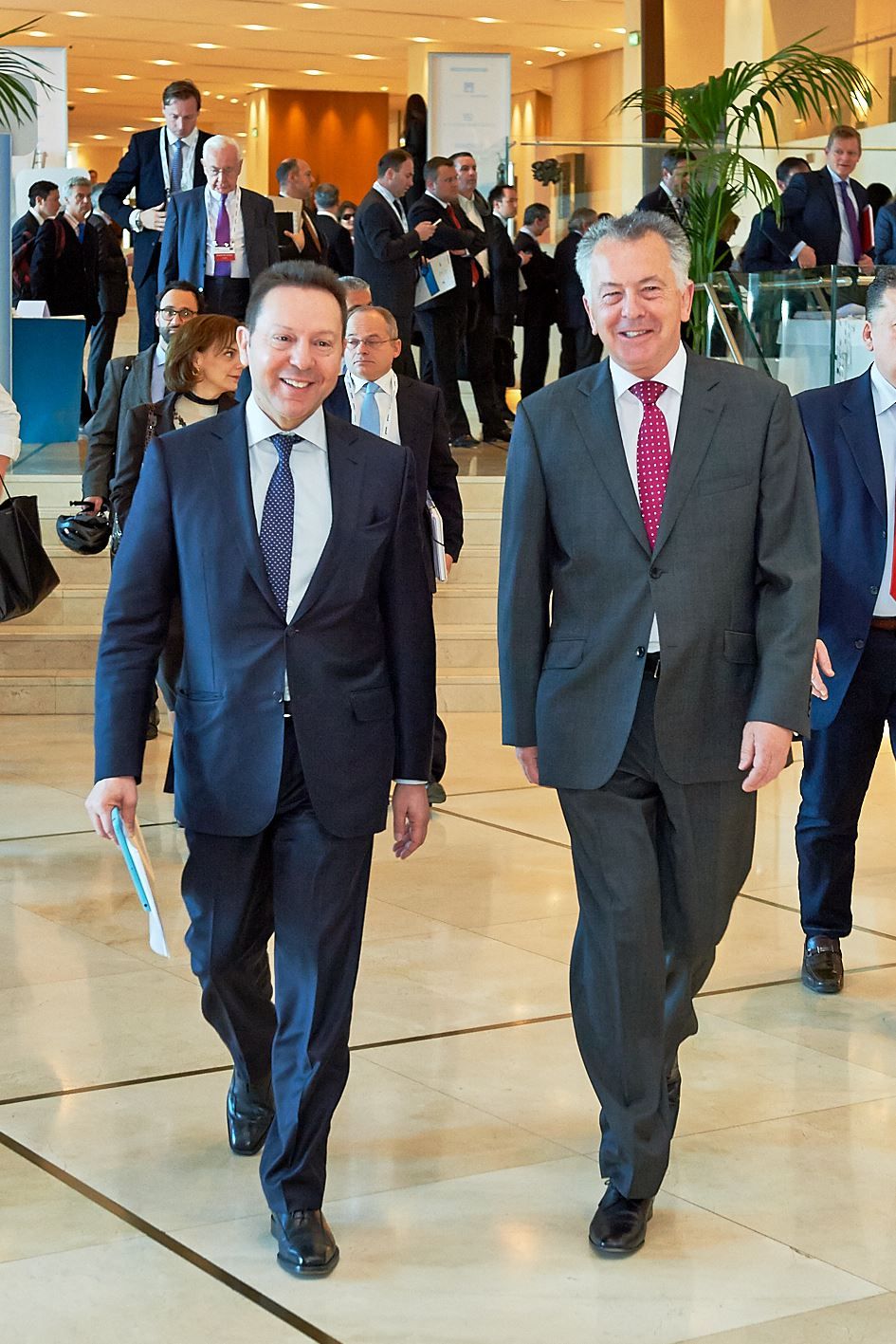 Group of executives in suits walking through a bright corporate lobby with modern decor.
