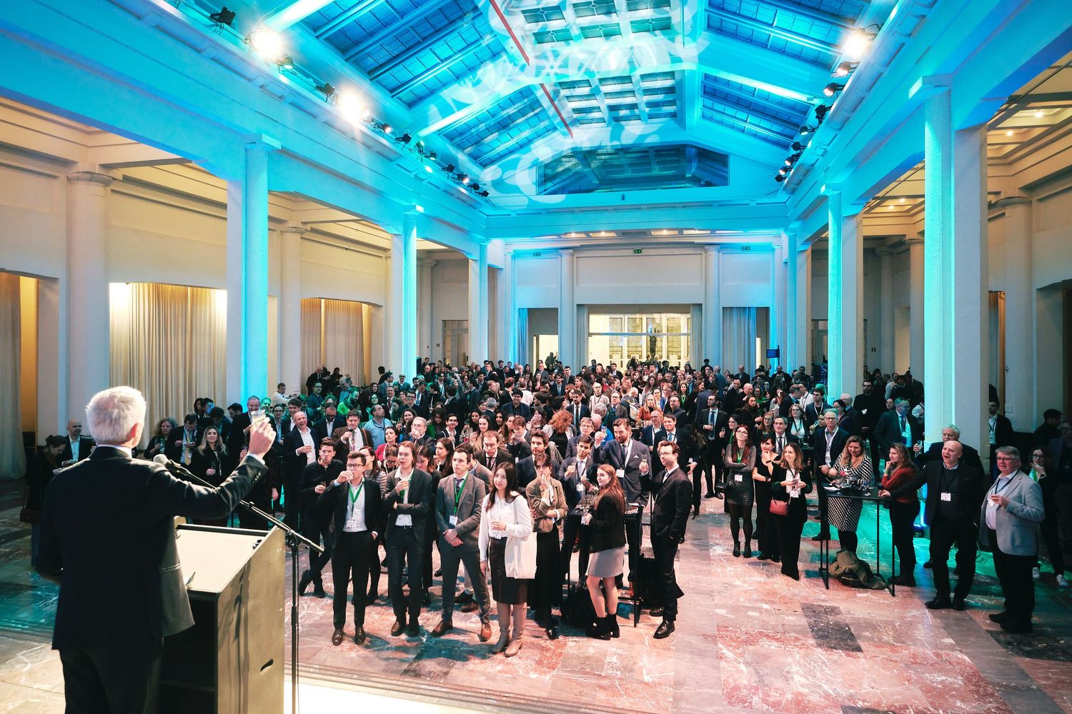 Large corporate event venue with blue lighting and crowd of attendees in formal attire.