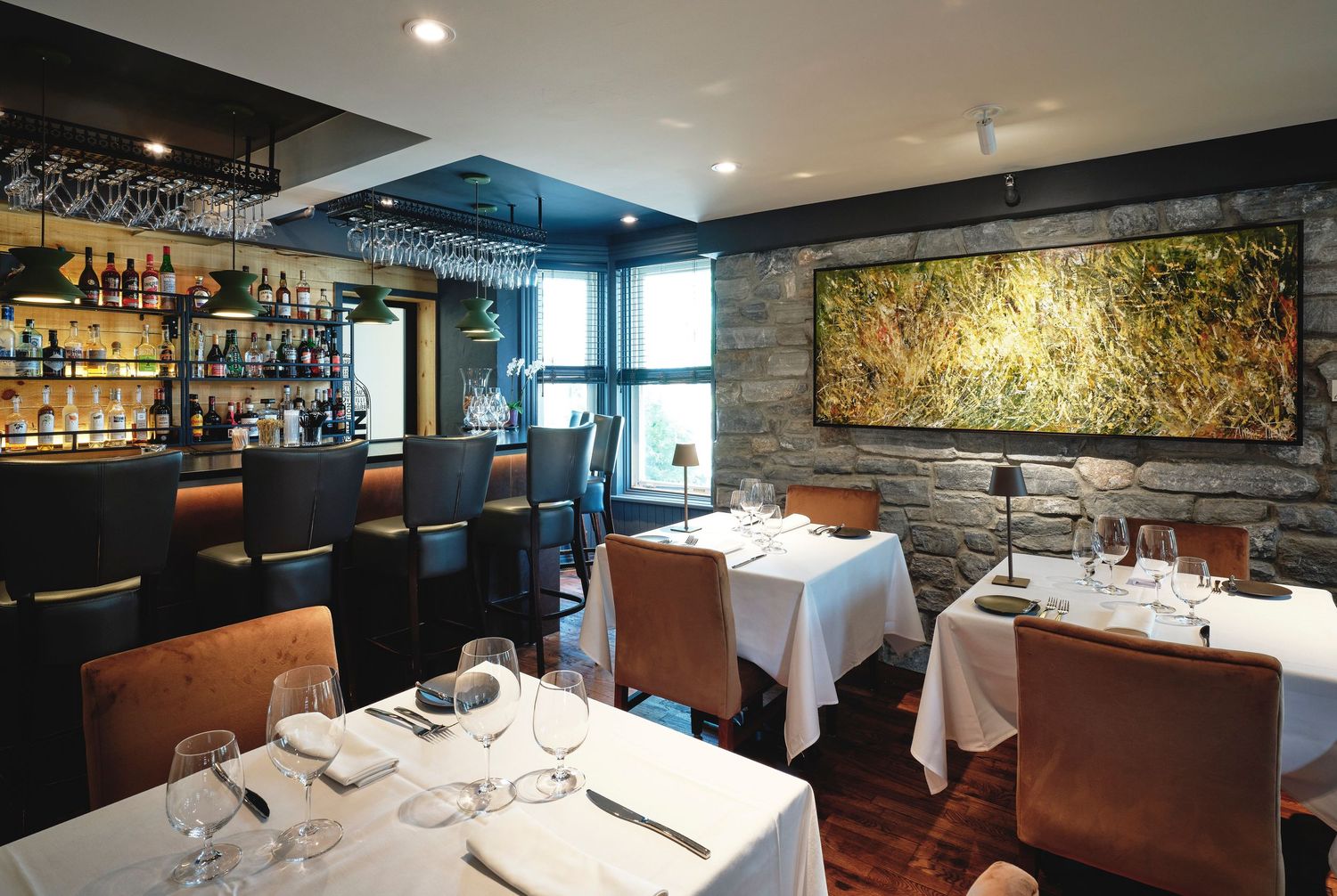 Sophisticated dining room with white tablecloths, brown leather seating, and stone accent walls.