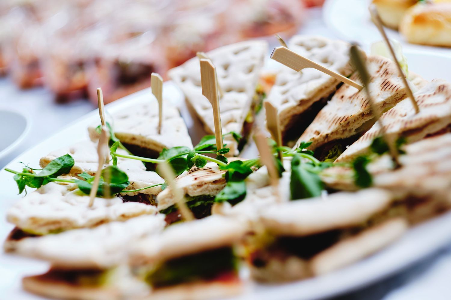 Sliced baguette topped with creamy spread and fresh herbs arranged on a white serving platter.