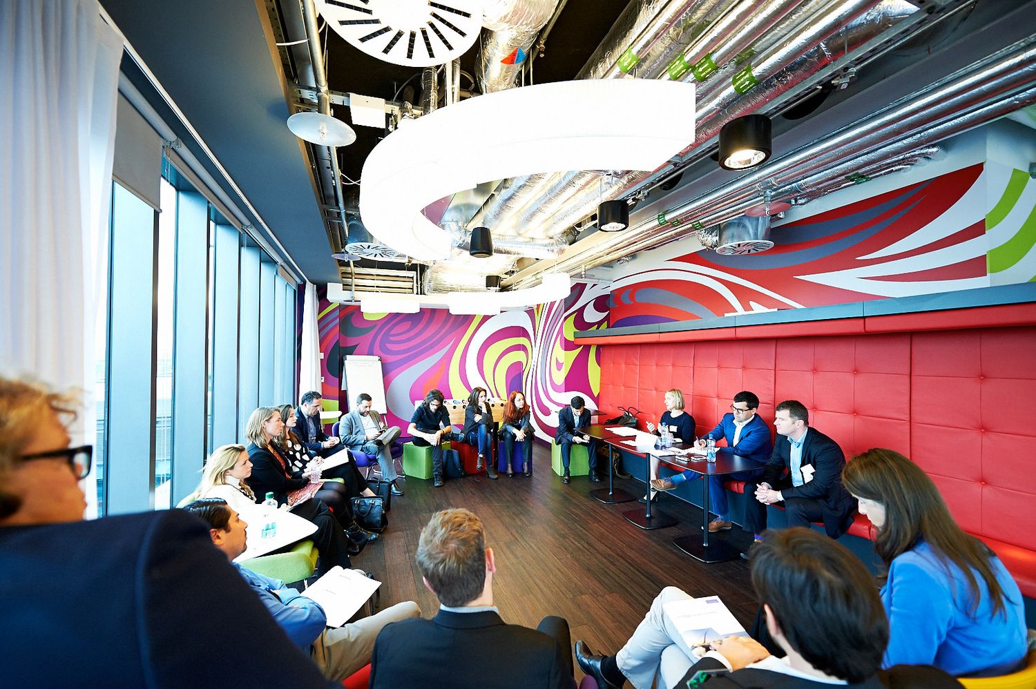 Business professionals seated in a modern conference room with colorful walls and large windows.