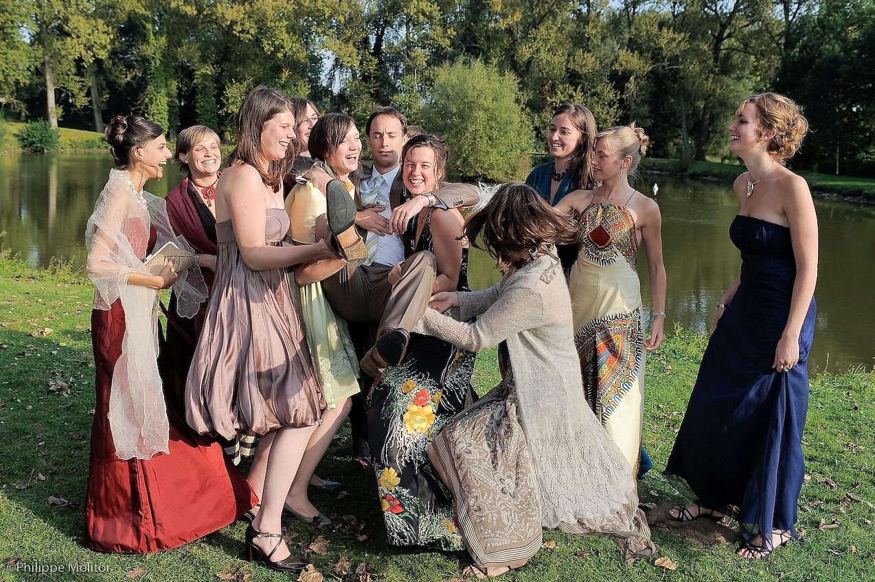 Bridesmaids in colorful gowns celebrate with the bride outdoors near a scenic pond.