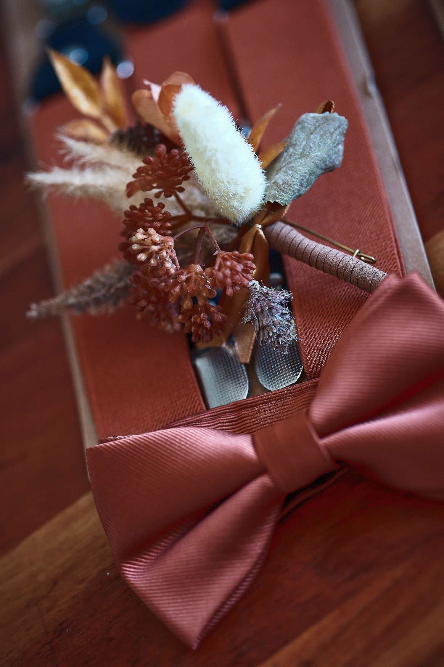 Elegant dusty rose bow tie and boutonniere with dried flowers displayed on a wooden surface for a wedding.