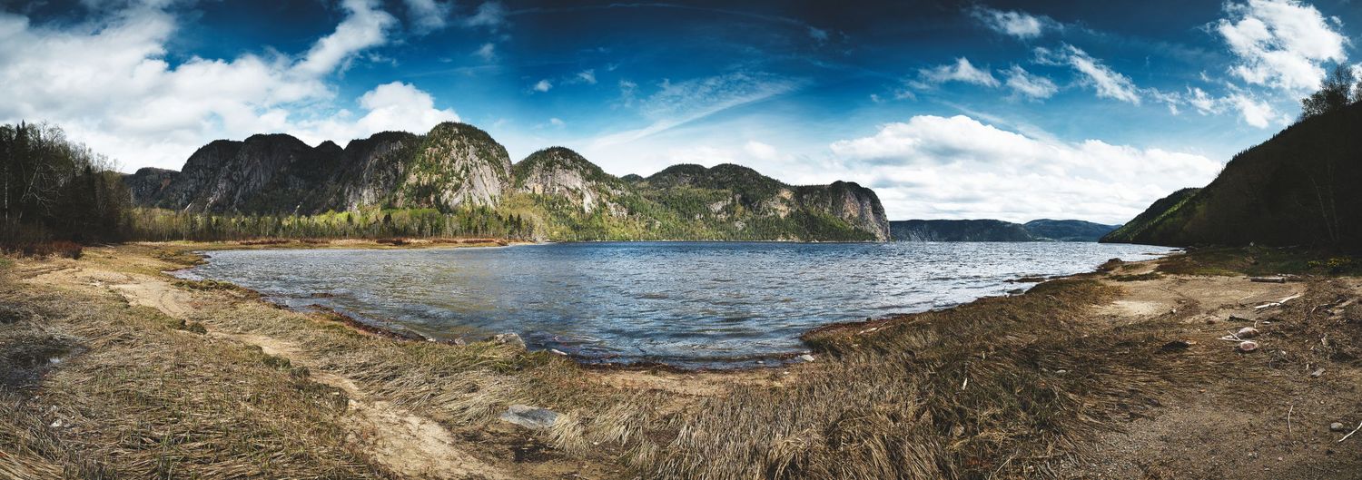 Wide panoramic vista of rugged mountain peaks and coastline under dramatic cloudy skies.
