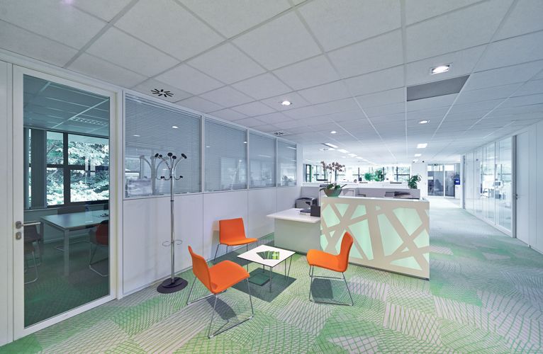 Contemporary office lounge area with orange chairs and glass partitions.