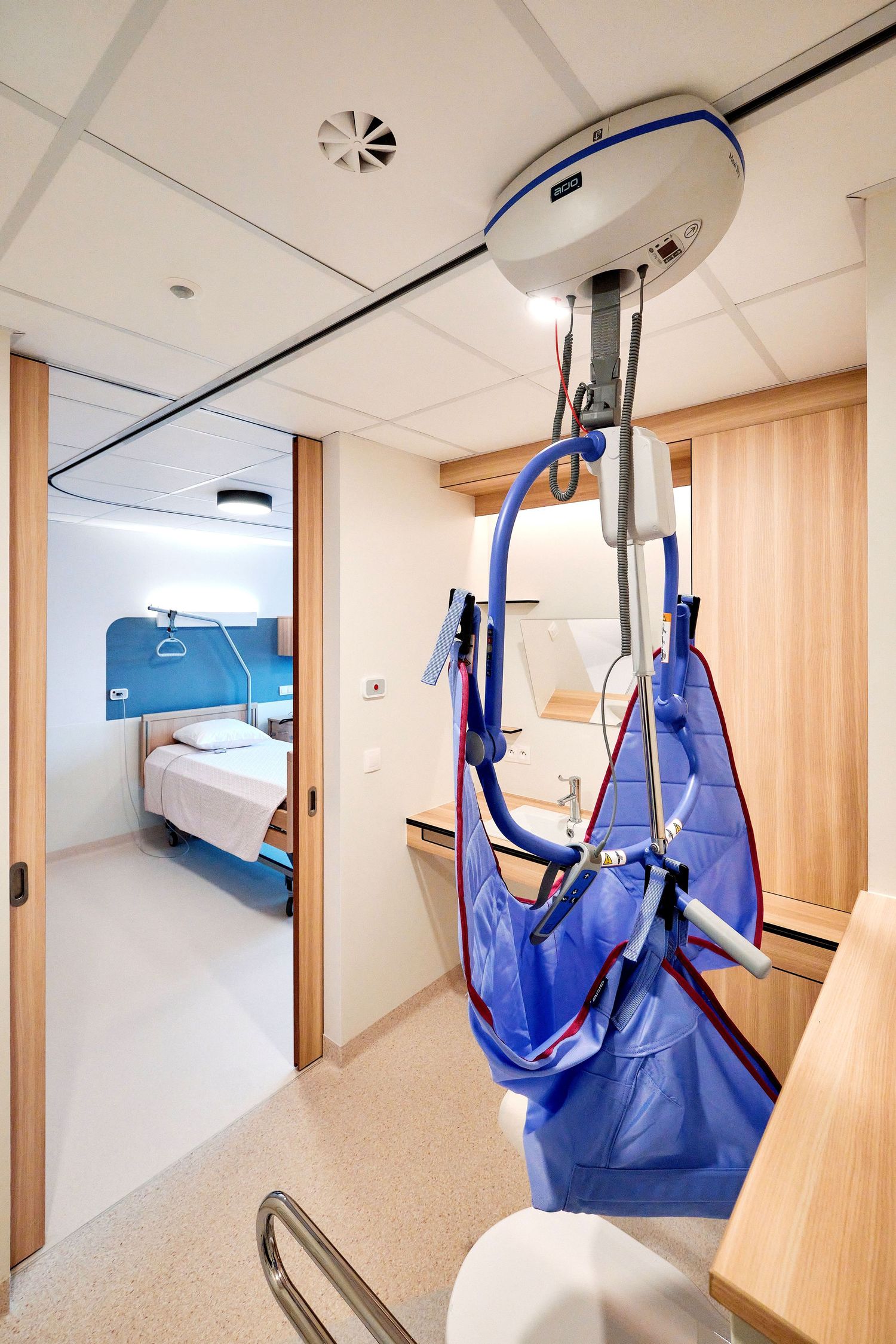 Hospital room corridor with blue patient lift equipment mounted on ceiling track.