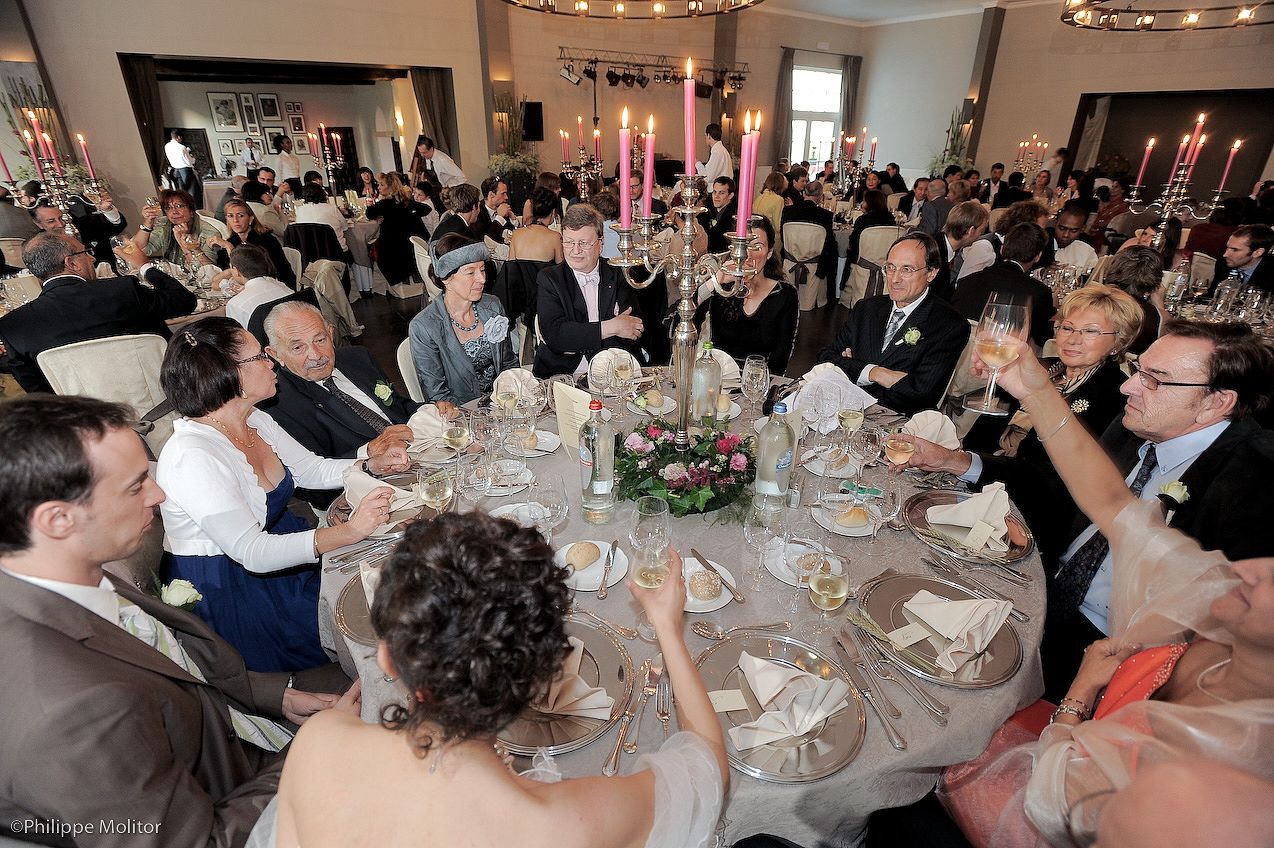 Guests raising glasses in a toast at an elegant wedding reception banquet with candlelit round tables.