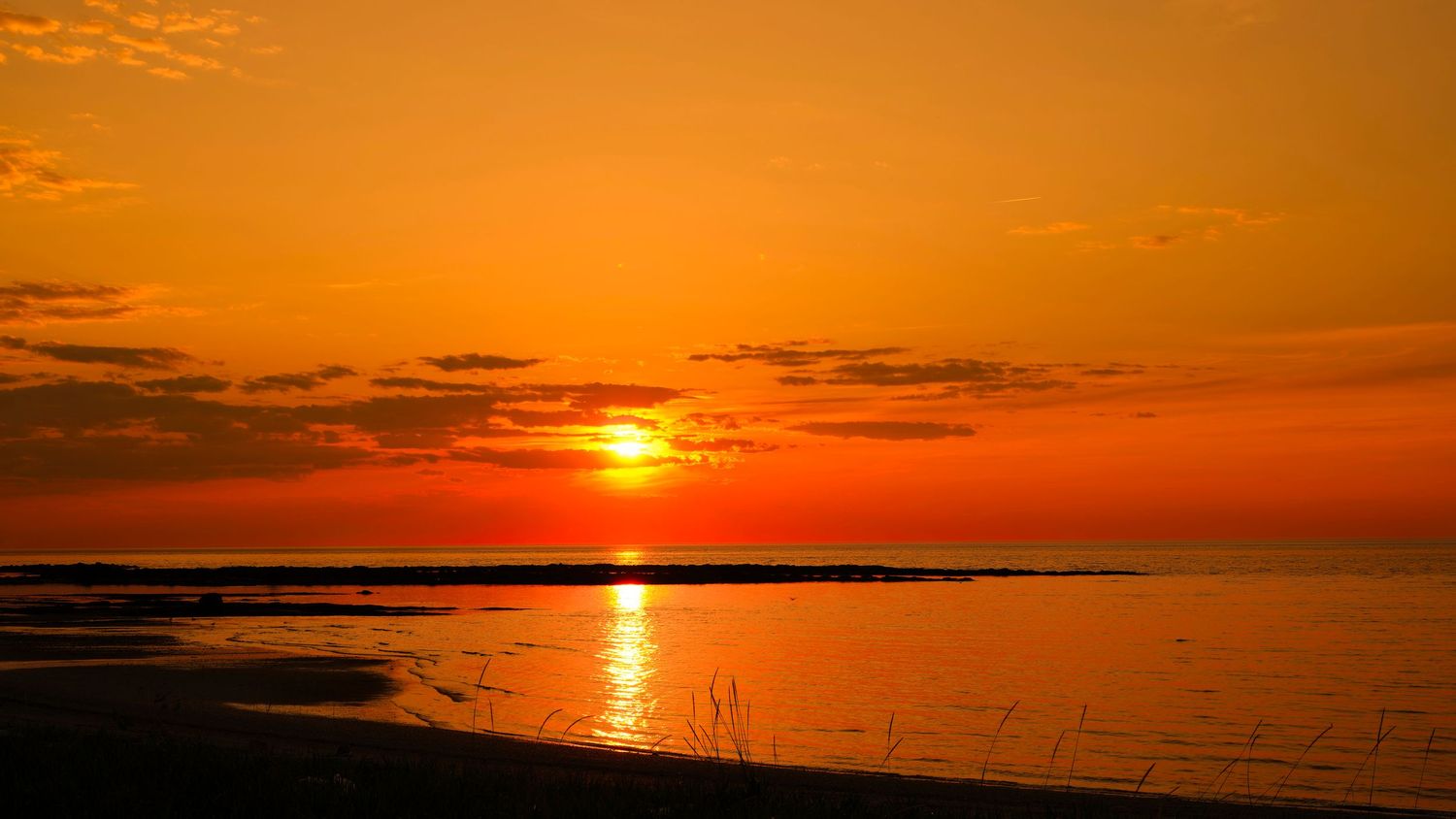 Dramatic orange sunset over water with sun reflection creating a golden path on the surface.