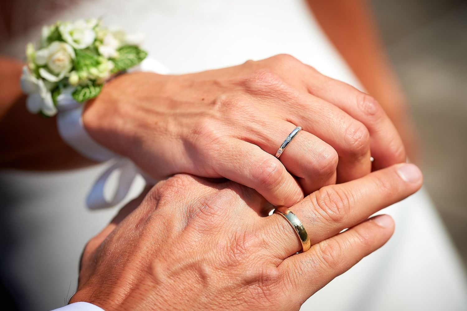 Close-up of elderly couple exchanging wedding rings, bride wearing floral wrist corsage during outdoor ceremony.