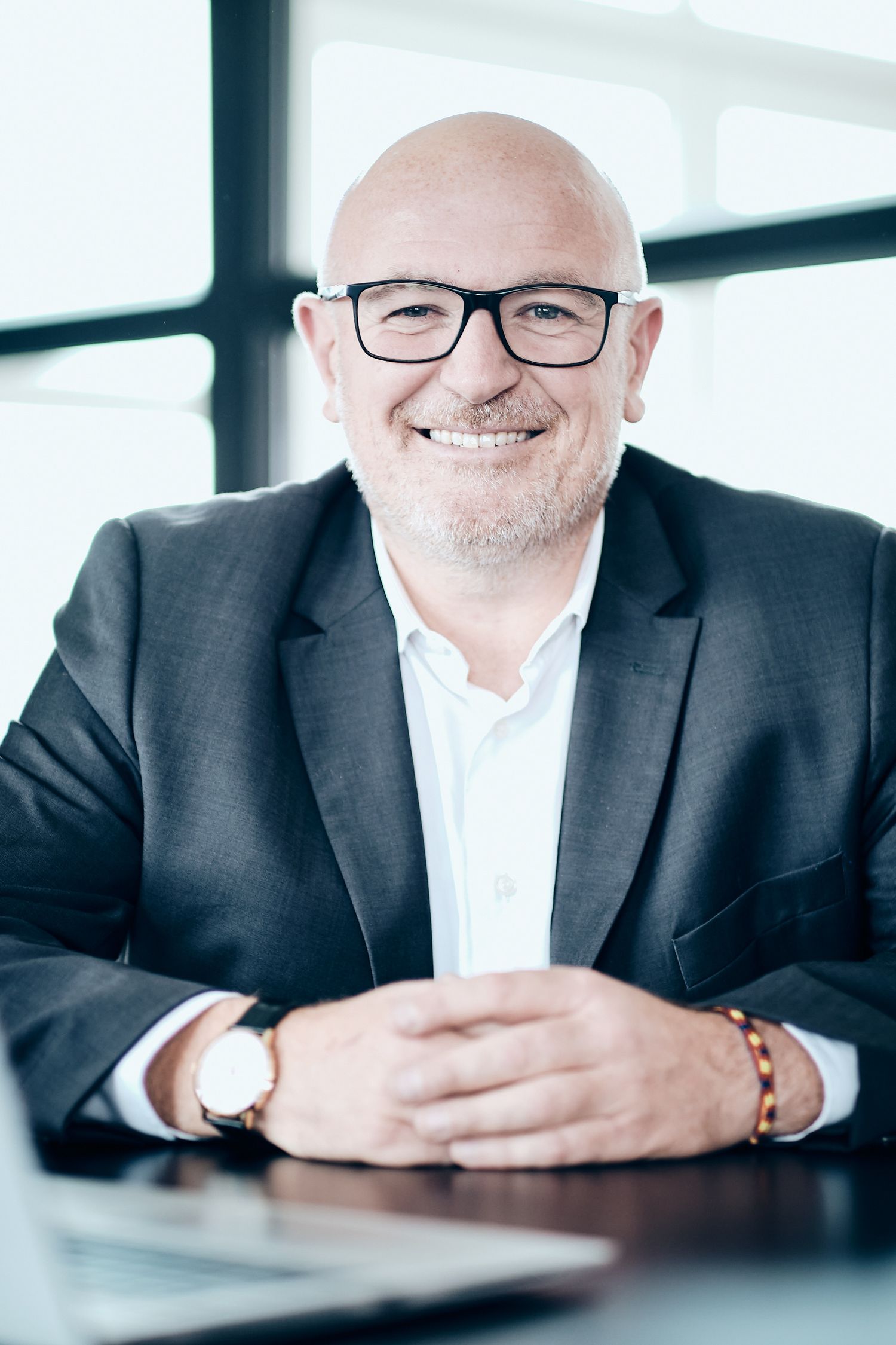 Corporate portraits of professional in dark suit and glasses at office desk.