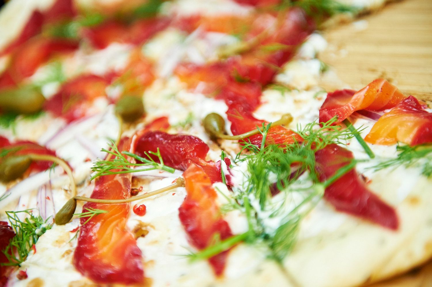 Fresh pizza topped with red meat, herbs and cheese on a wooden serving board.