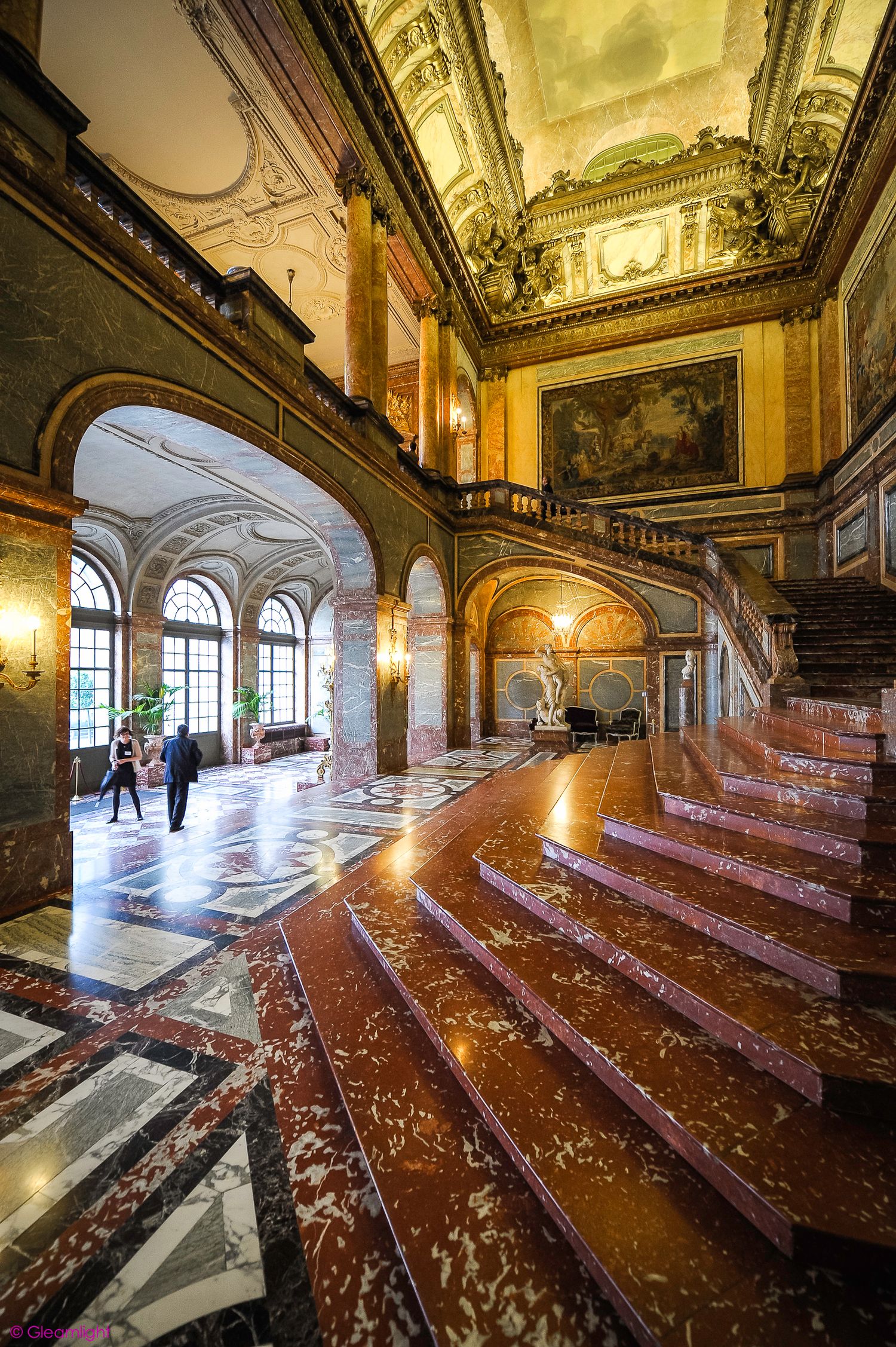 Grand ballroom with polished wooden floors and ornate ceiling featuring tiered seating arrangement.