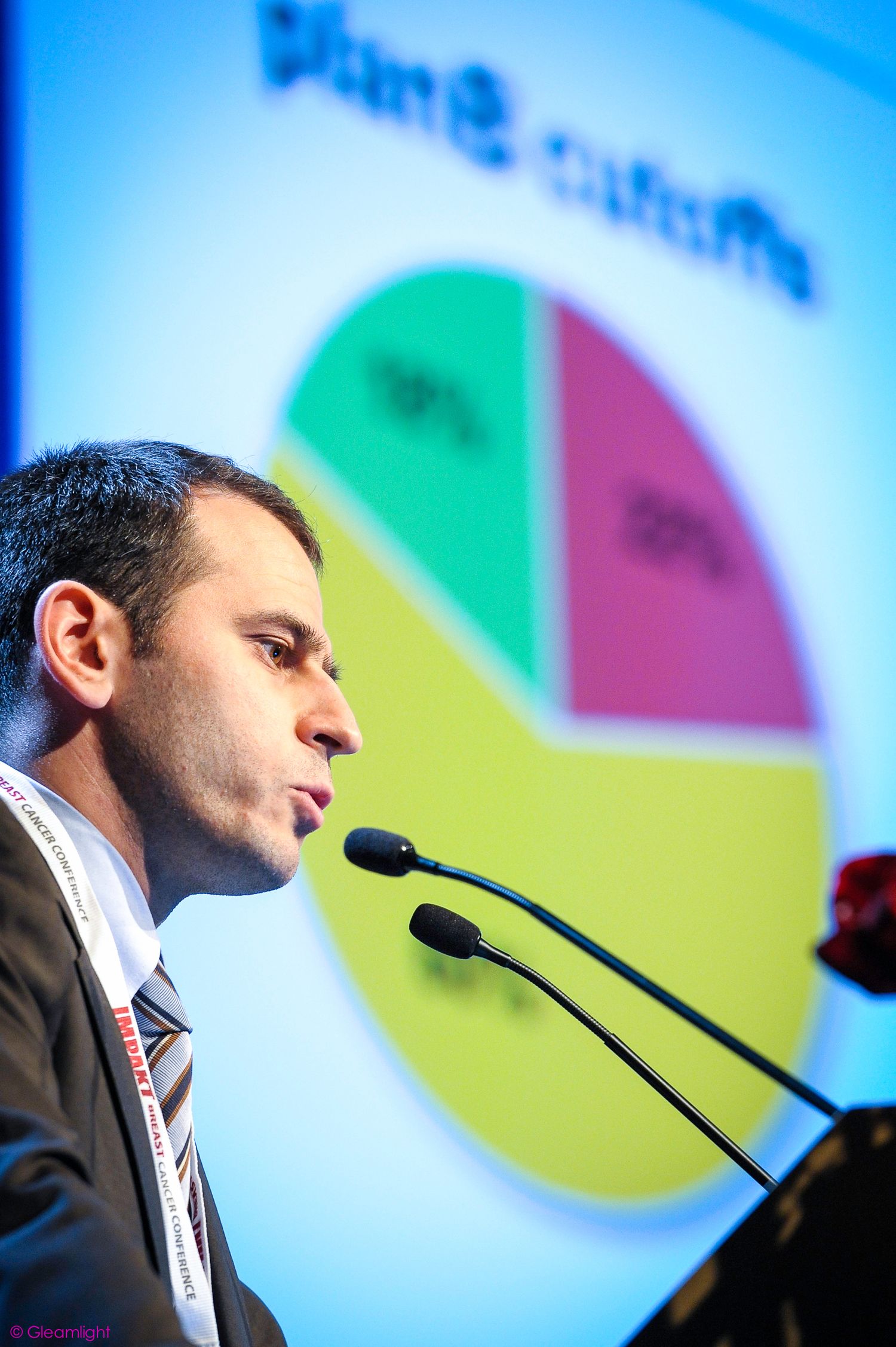 Presenter speaking at podium with colorful pie chart projected in background.