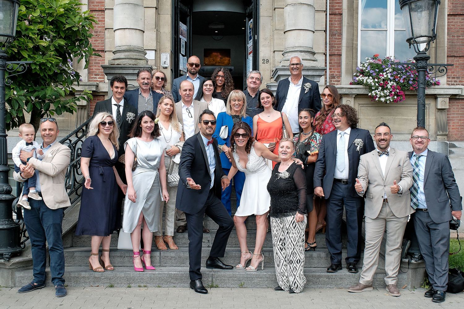 Large group of elegantly dressed guests posing on stone steps outside a historic building at a wedding celebration.