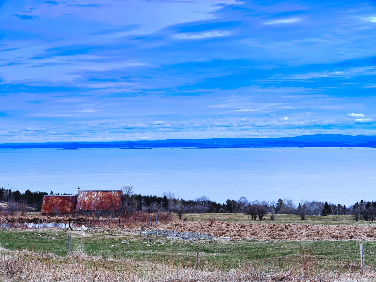 Panoramic view of a rural landscape with blue sky, scattered clouds, and distant tree lines stretching across the horizon.