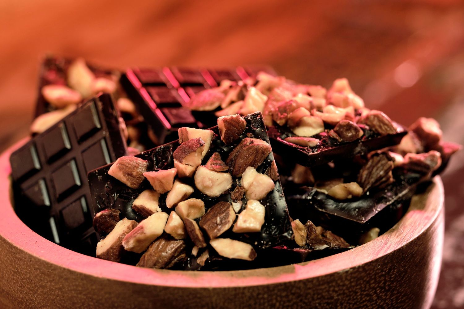 Dark chocolate pieces with nuts arranged on pink-lit surface.