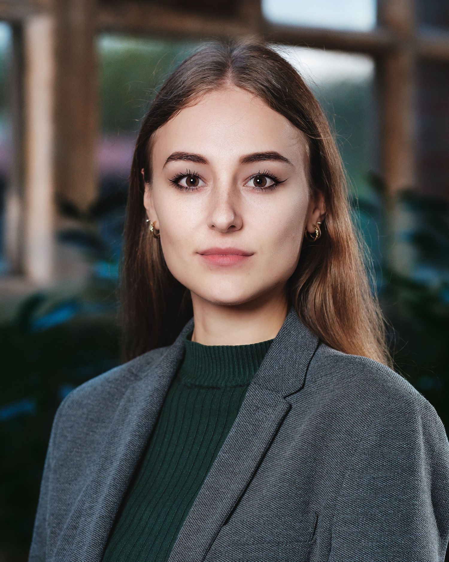 Professional in grey blazer and dark top photographed in office environment.