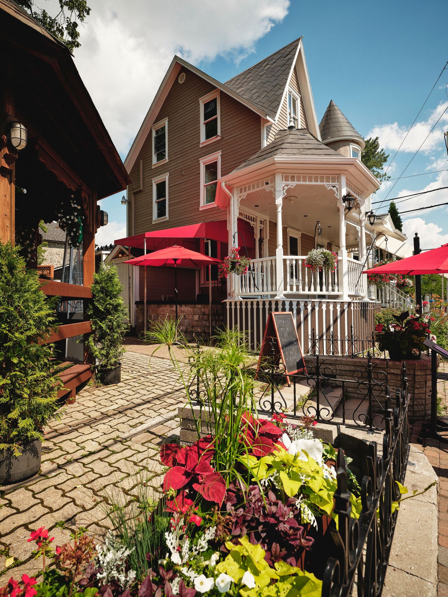 Victorian-style restaurant patio with red umbrellas and colorful flower gardens.