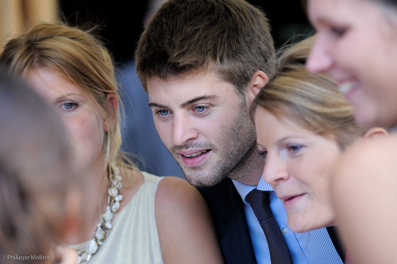 Young man in blue tie surrounded by blonde women at a formal event, engaged in conversation.