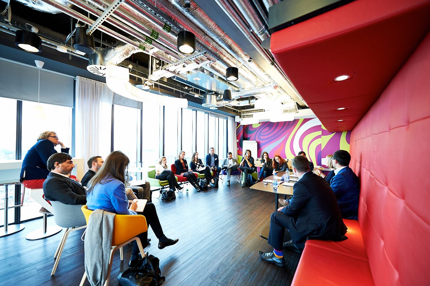 Corporate meeting space with red walls and large windows showing attendees in discussion.