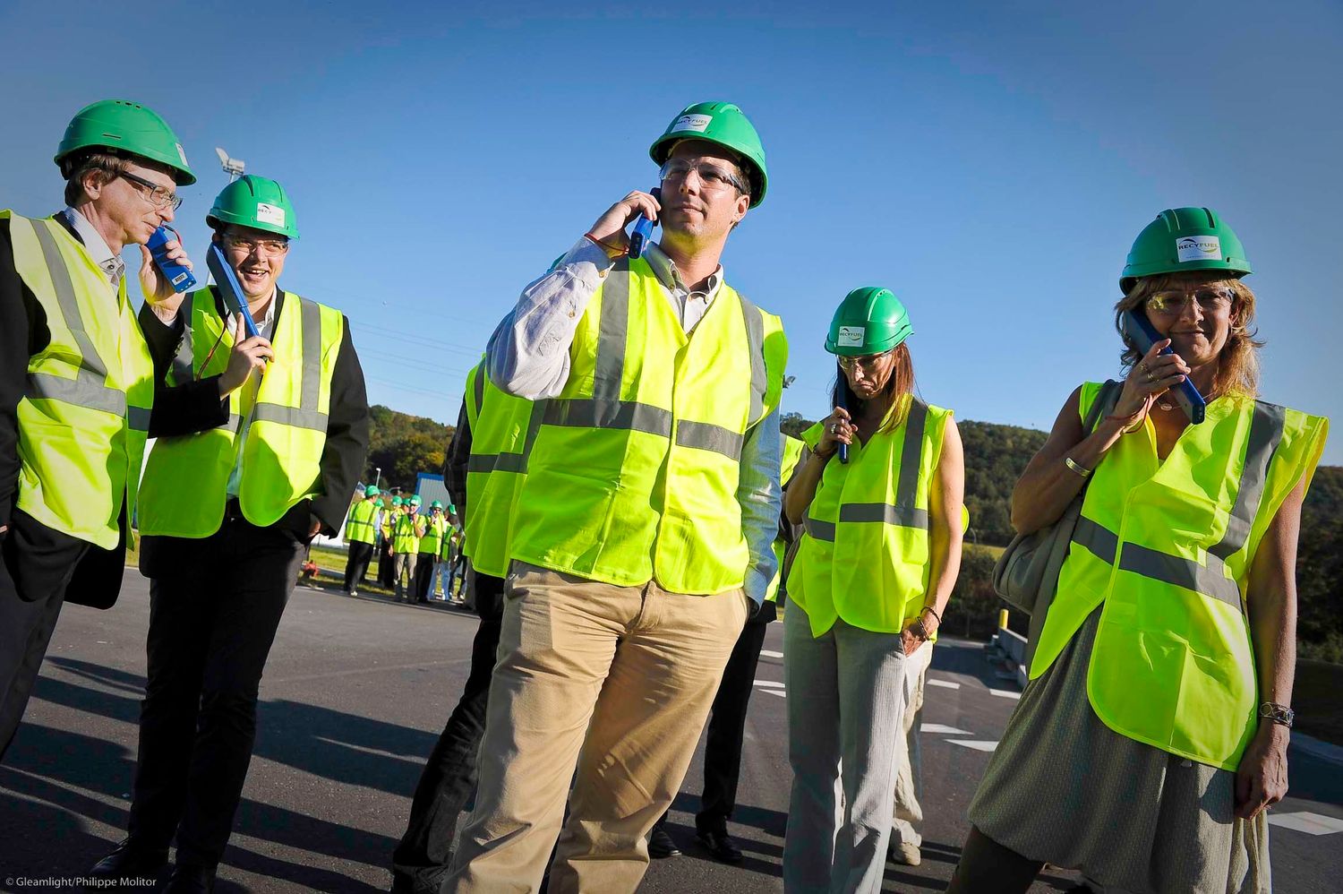Group of workers wearing green hard hats and reflective safety vests outdoors.