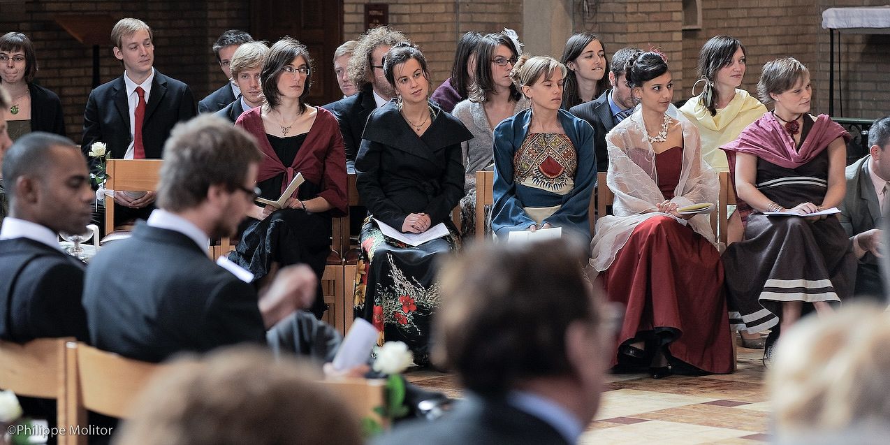 Guests seated in church pews during a formal wedding ceremony, dressed in elegant attire.