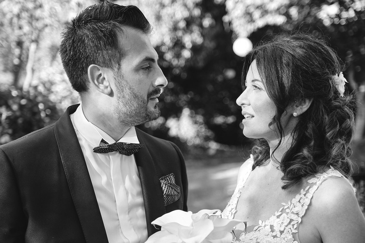 Black and white wedding photo of a smiling bride and groom in formal attire looking at each other outdoors.