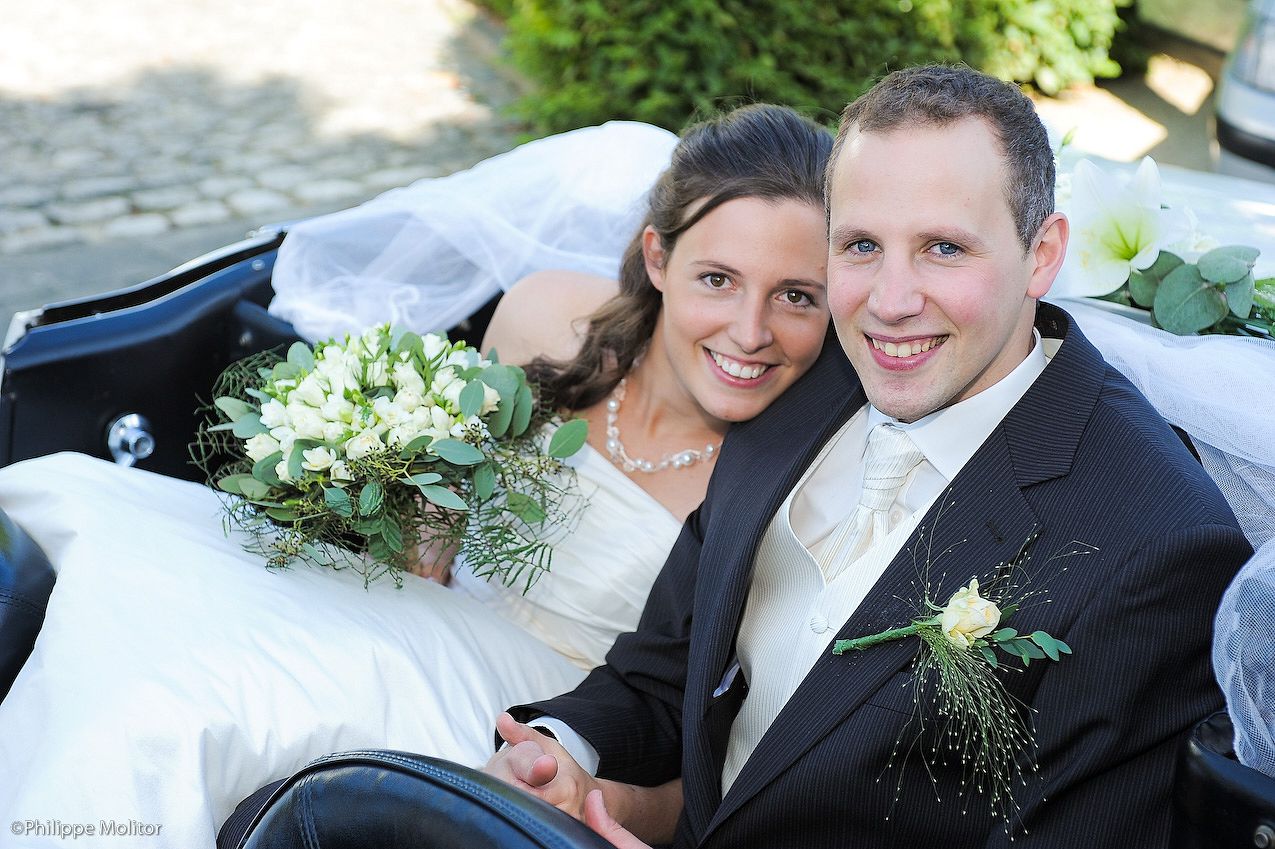 Happy newlywed couple smiling in a wedding carriage, bride holding white bouquet, groom in black suit with boutonniere.